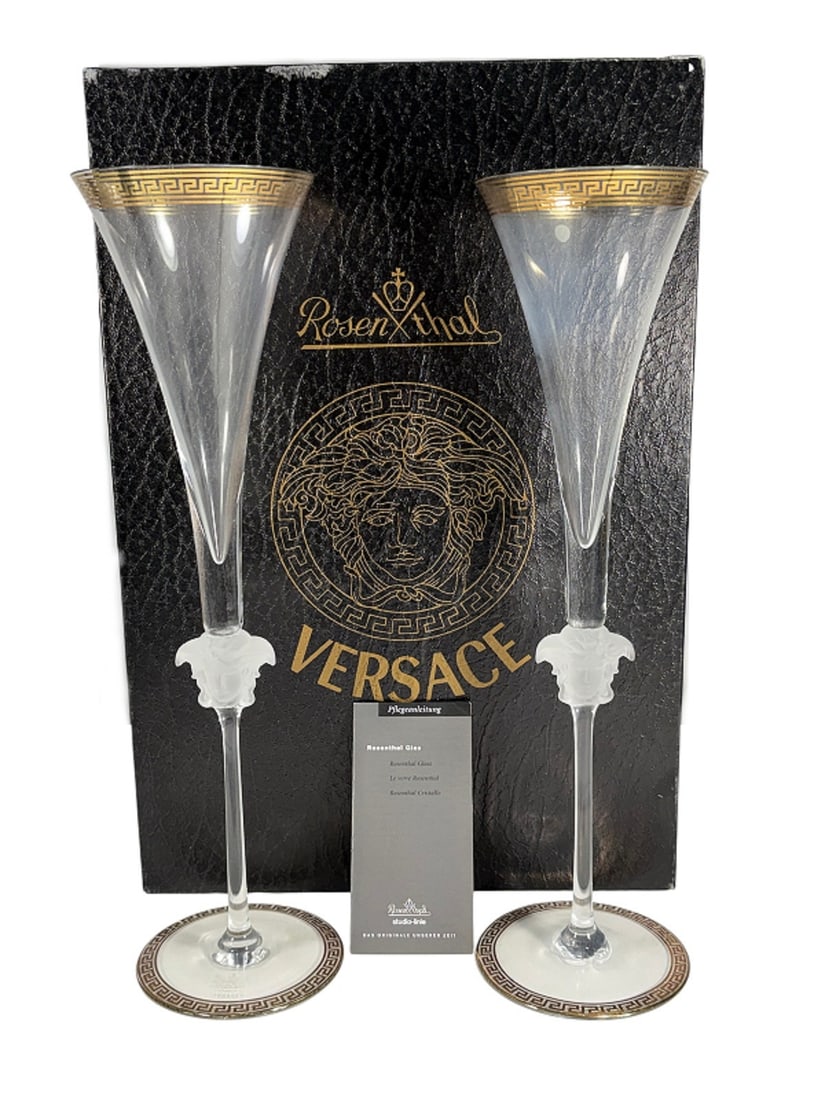 Rosenthal Versace Medusa D'Or Champagne Flutes 2pc: Rosenthal for Versace pair of Medusa d'Or crystal champagne flutes. Frosted Medusa head stems. Wide bases with gilt Greek key meander border. Flared bowls with gilt rim and black detailing. Etched