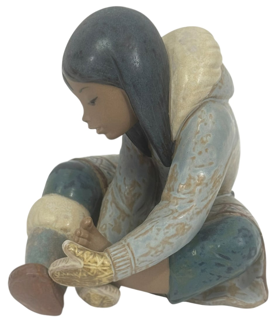 Lladro Eskimo Girl w/ Cold Feet Porcelain Figurine: Lladro Spanish porcelain figurine titled 'Eskimo Girl with Cold Feet' model number 2157. This piece portrays a young Inuit girl seated with one leg pulled up, gently warming her bare foot with her