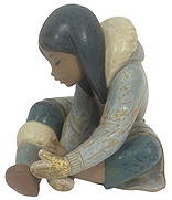 Lladro Eskimo Girl w/ Cold Feet Porcelain Figurine: Lladro Spanish porcelain figurine titled 'Eskimo Girl with Cold Feet' model number 2157. This piece portrays a young Inuit girl seated with one leg pulled up, gently warming her bare foot with her