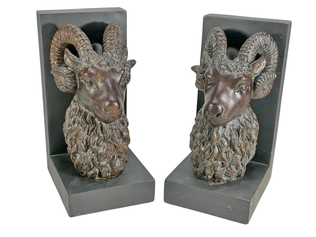 Pair of Ram Head Patinated Resin & Wood Bookends: Pair of ram head bookends with curled horns and textured detail, mounted on rectangular wood bases. Each piece measures approximately 7.75 inches tall by 3.75 inches wide by 4.75 inches deep.Condition