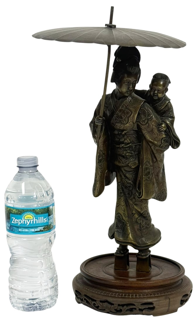 Japanese Bronze Sculpture of a Geisha w/ Child: Japanese bronze sculpture depicting a geisha carrying a child on her back beneath a large parasol. The figures are finely detailed, with the geisha in a traditional floral kimono and elevated geta san