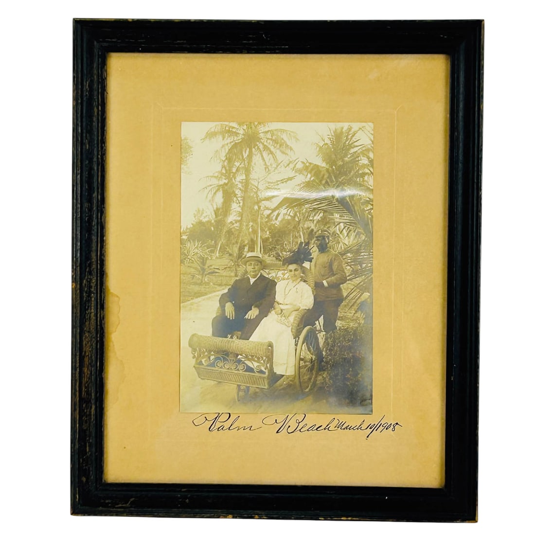1908 Palm Beach Sepia Tone Photographic Print: A black and white photograph print dated March 10, 1908, depicting individuals posed outdoors in Palm Beach, Florida. Image shows palm lined setting with figures seated and standing near a wicker benc
