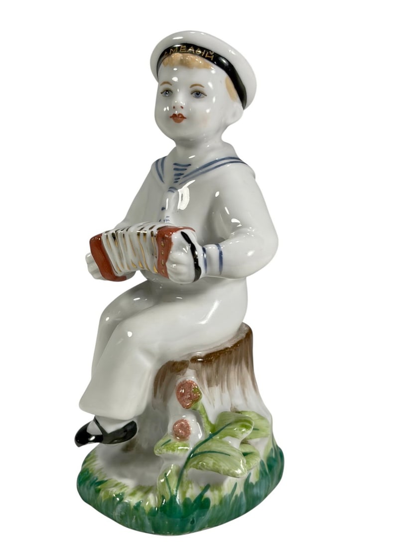USSR Sailor Playing Accordion Porcelain Figurine: USSR porcelain sailor figurine, modeled seated on a tree stump and playing an accordion. Finished in a white naval uniform with blue trim and black shoes, with a gilt-inscribed cap band. Underside