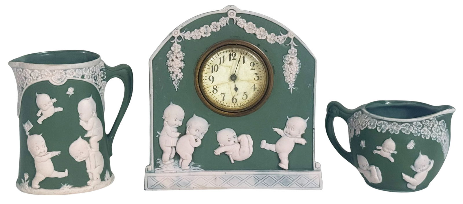 Rose ONeill Kewpie Jasperware 3pc LOT SIGNED: Three-piece jasperware set featuring Rose ONeills iconic Kewpie characters in detailed white relief against a matte green ground. The lot includes a mantel clock, pitcher, and creamer, each decorated