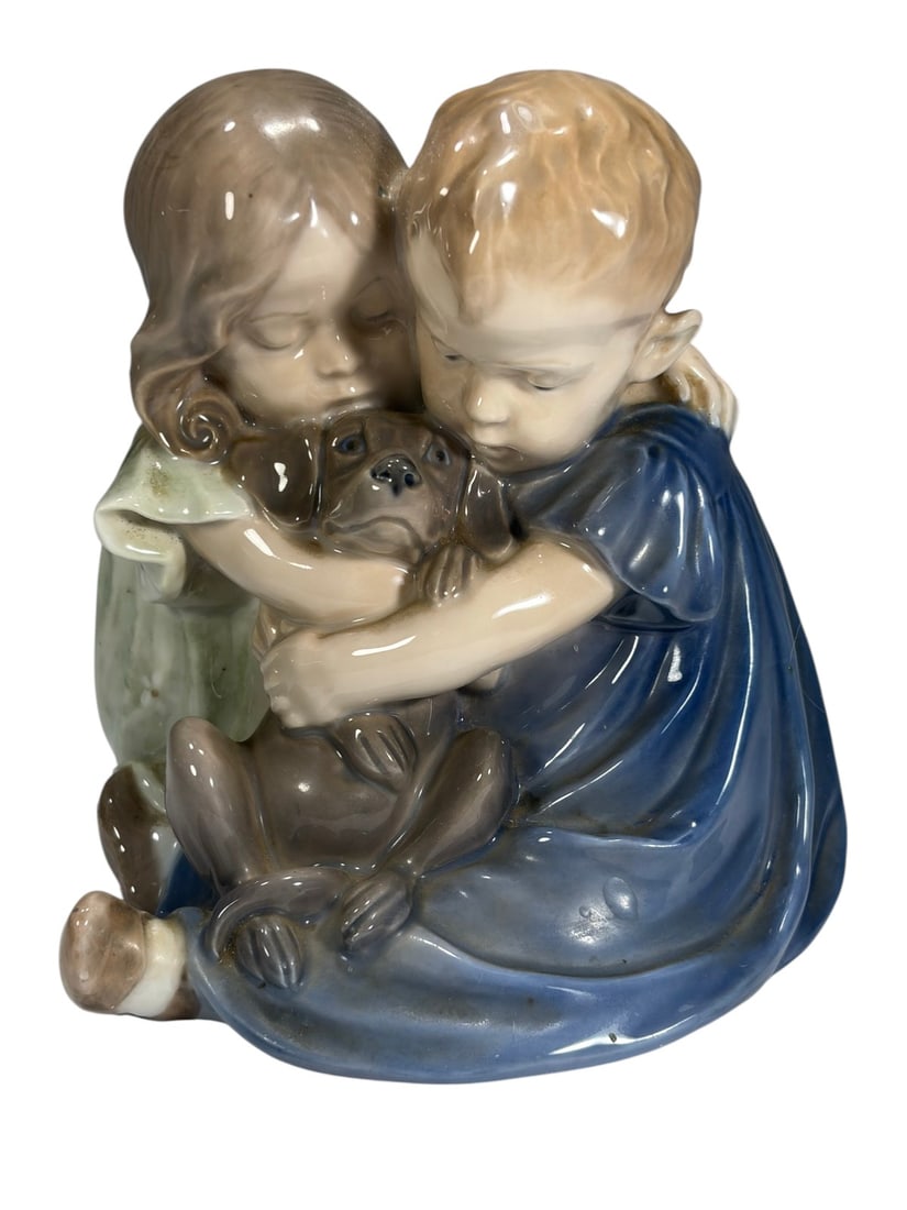 Royal Copenhagen Hugging Dog Porcelain Figurine: Royal Copenhagen Denmark porcelain figure of two children seated together hugging a small dog. Boy in blue and girl in pale green with soft naturalistic glazing, dog in warm brown tones with expressiv