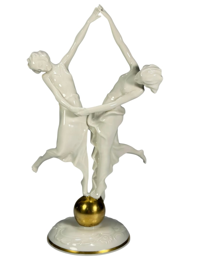 Hutschenreuther Dancing Girls by Karl Tutter Fig: Hutschenreuther porcelain Dancing Girls figurine designed by Karl Tutter. Two Art Deco dancers with elongated forms and flowing garments, standing atop a gilt sphere with arms raised and hands joined,