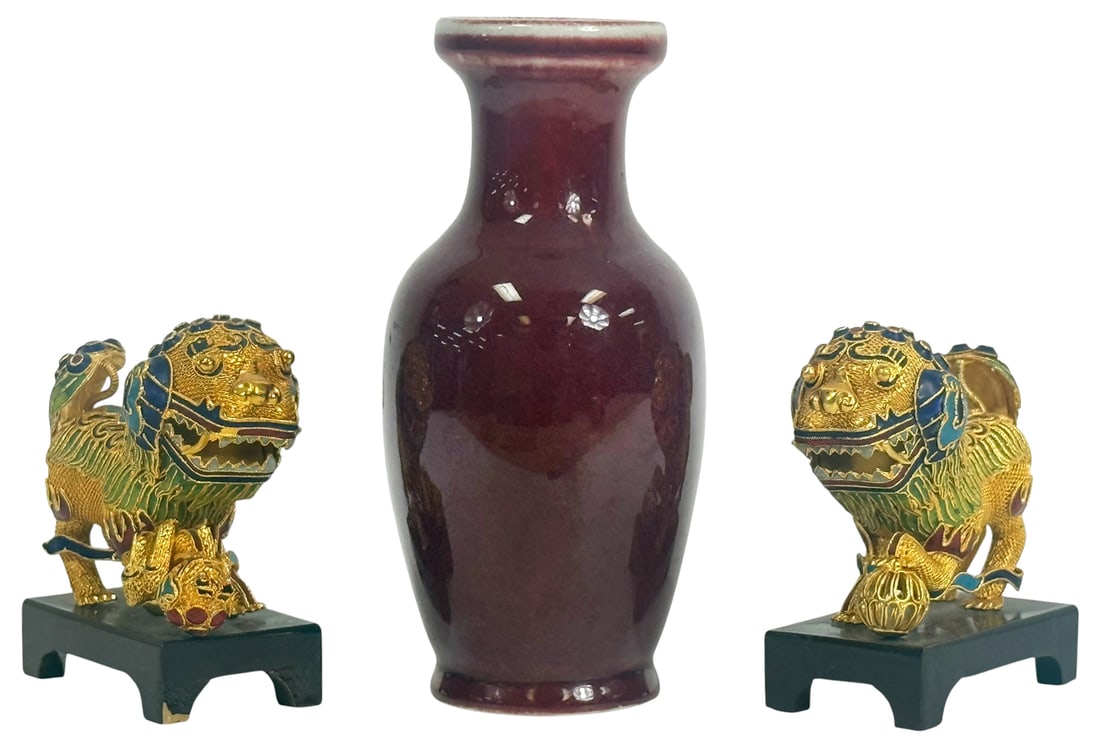 Chinese Cloisonne Foo Dogs & Sang de Boeuf Vase: Grouping of three Chinese decorative items including a pair of cloisonne enamel foo dog figurines, each finely detailed in gilt and multicolored enamel, posed with front paws on brocade balls and moun