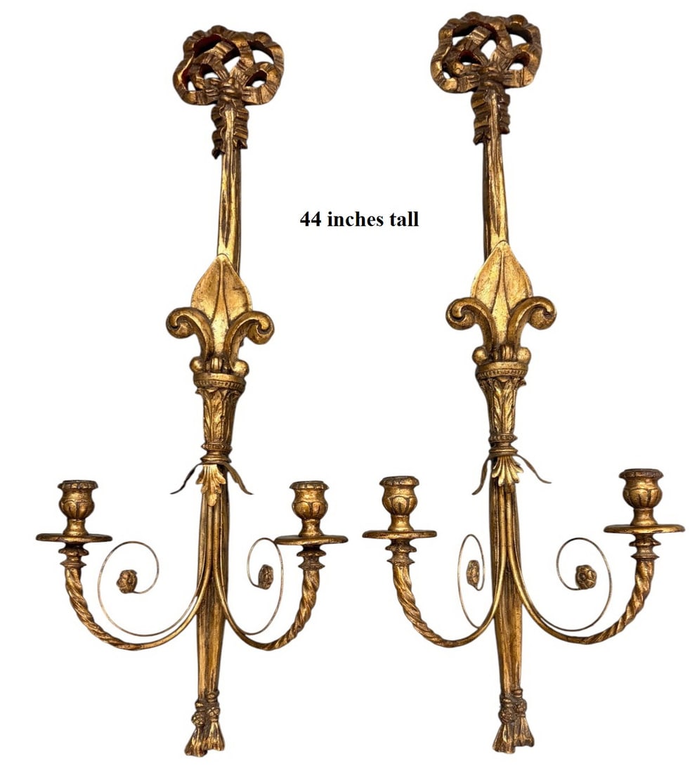 Louis XVI Style Gilt Fiberglass Wall Sconces 2pcs: Louis XVI style pair of gilt fiberglass two light wall sconces with ribbon crest, fluted foliate standard, central fleur de lis, and scrolled candle arms with drip pans. Antiqued gilt finish with tass