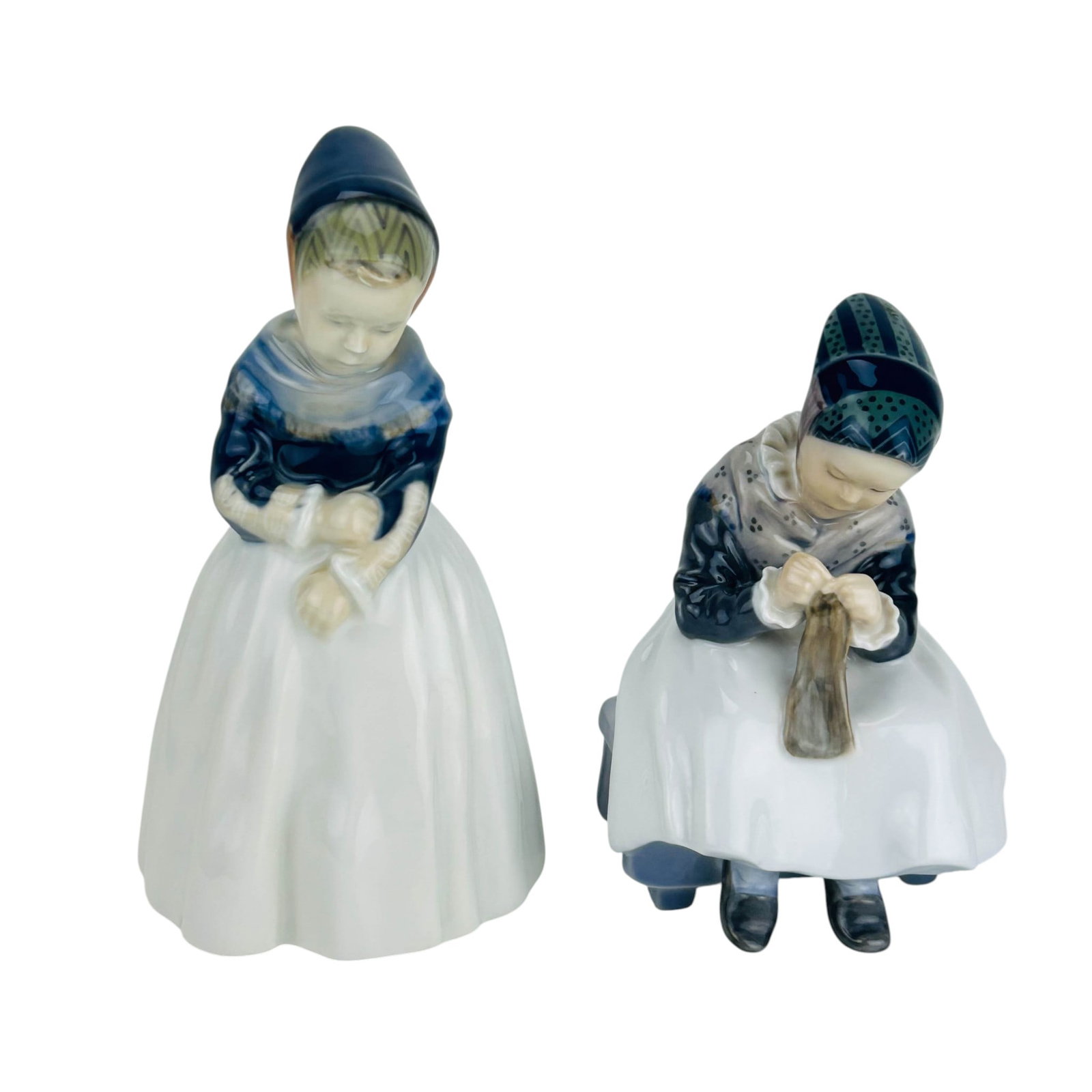 Royal Copenhagen Denmark Amager Girl Figurines 2pc: Royal Copenhagen Danish porcelain figurines, lot of two. Includes Amager Girl Sewing #1314 (Seated Child Knitting) and Amagaer Girl #1251 (Standing Girl in Regional Attire looking Down). Both designed
