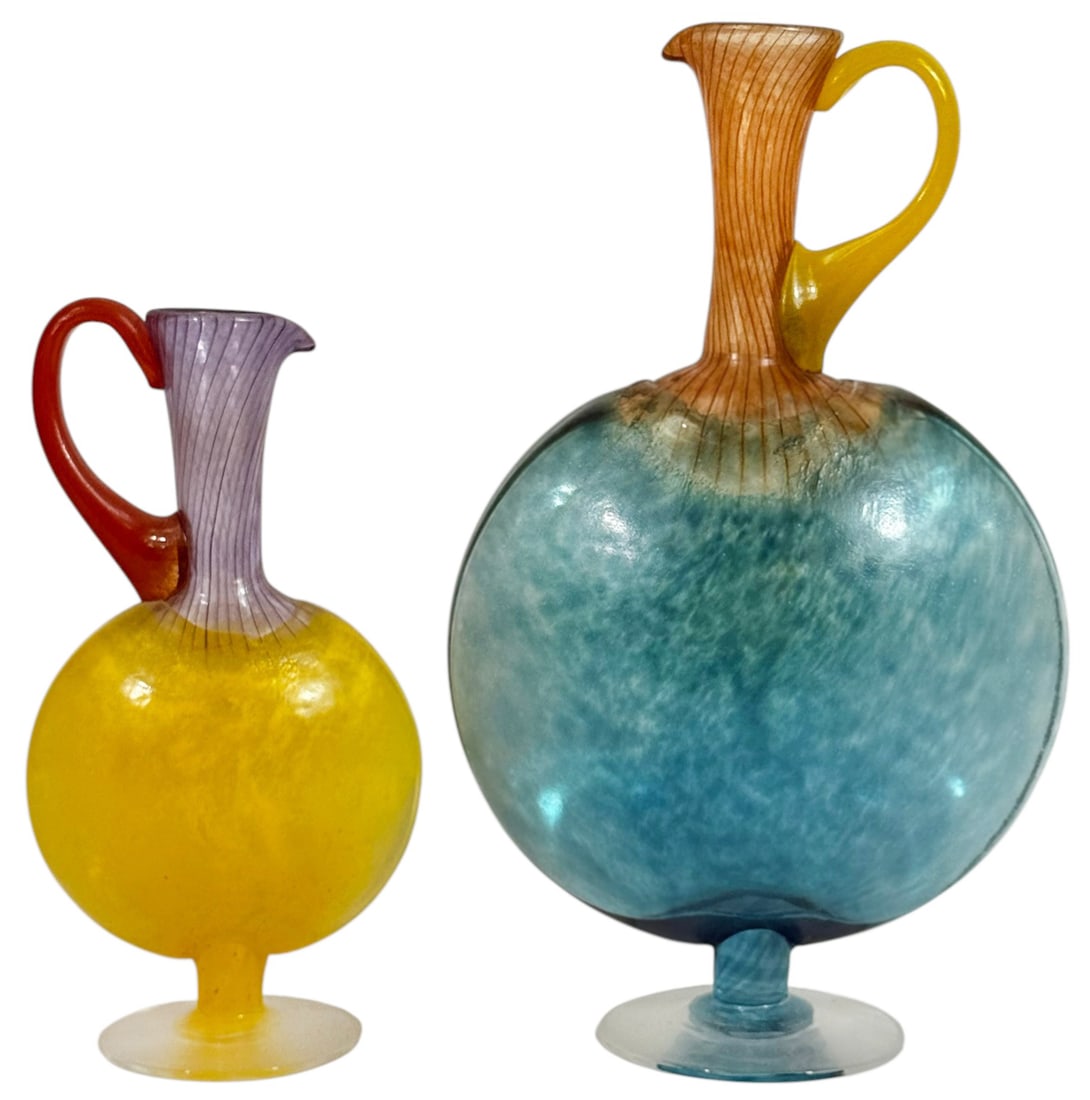 Pr of Bon Bon Jugs by Kjell Engman for Kosta Boda: Pair of hand-blown art glass "Bon Bon" jugs designed by Swedish artist Kjell Engman for Kosta Boda. Featuring disc-shaped bodies with applied handles and fluted necks, the larger jug displays a gradie