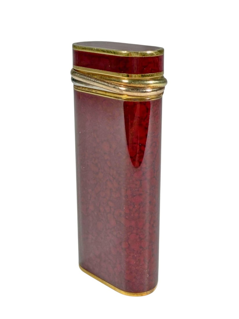 VTG Cartier Paris Trinity Red Lacquer Lighter: Cartier Paris Trinity red lacquer lighter with mottled red body, gold plated trim, and triple band detail. Slim curved rectangular form with hinged lid and flint wheel ignition. Base is stamped 'Carti
