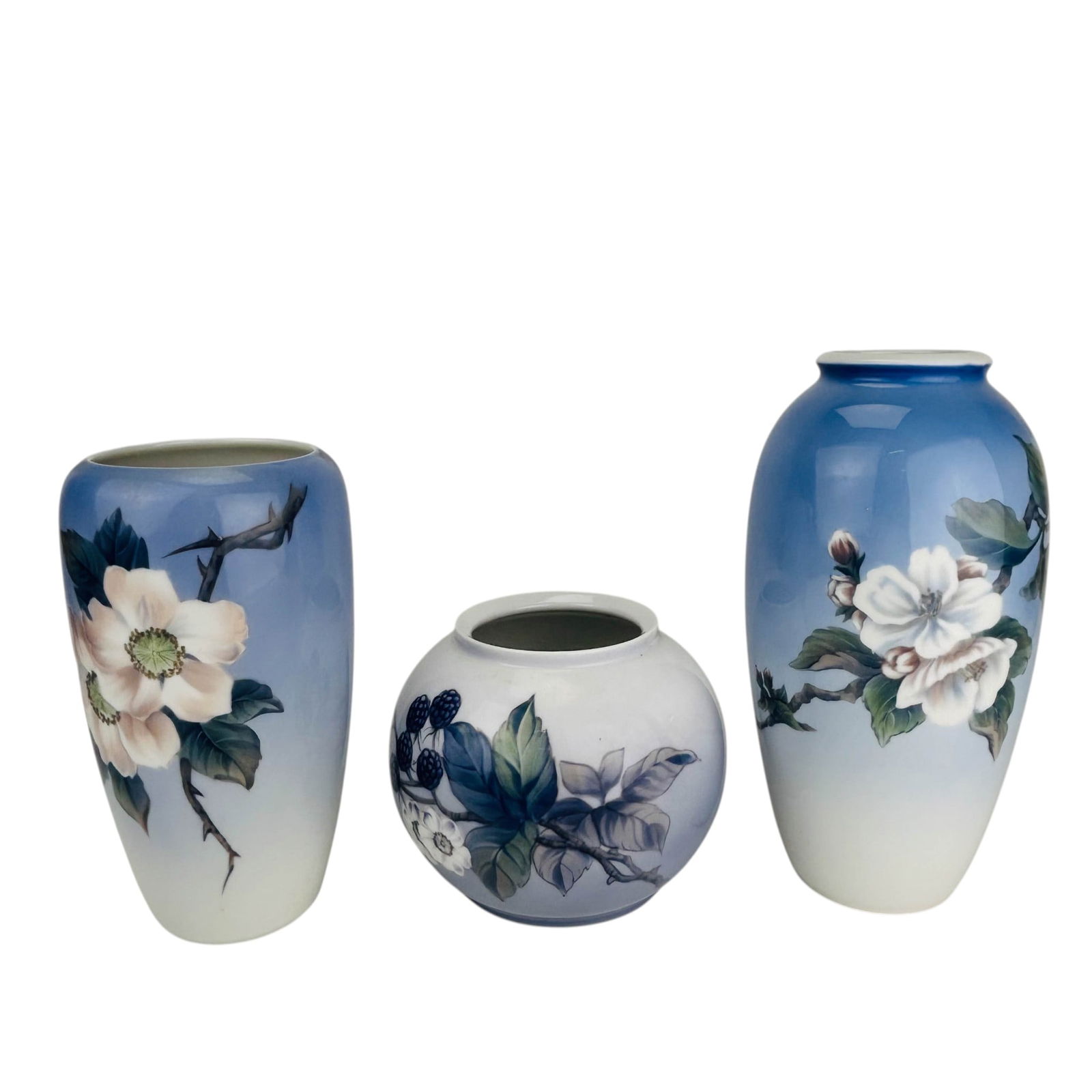 Royal Copenhagen Floral Butterfly Berry Vase 3pc: Royal Copenhagen Denmark porcelain vase grouping of, three pieces. Two tall vases display magnolia blossoms with shaded foliage and butterfly accents. The rounded low-form vase is decorated with black