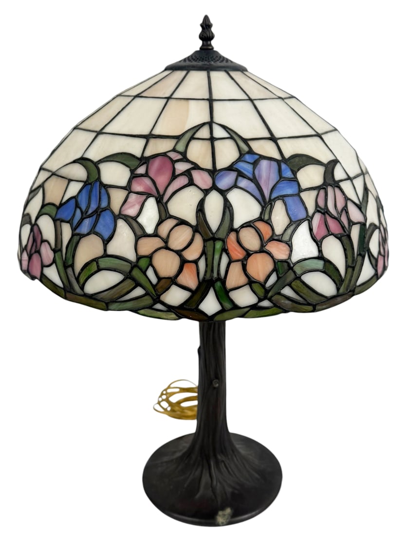 Tiffany Style Floral Stained Glass Table Lamp: Tiffany style table lamp featuring a stained glass shade decorated with a floral motif in blue, pink, and peach tones with green stems and leaves. The domed leaded glass shade sits on a dark bronze to