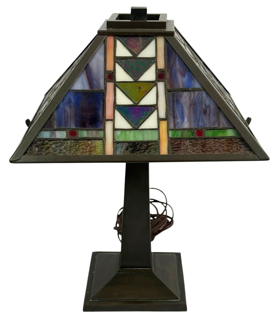Arts & Crafts Style Stained Glass Table Lamp: Arts and Crafts style table lamp featuring a geometric stained glass shade with multicolor panels and iridescent glass accents. The pyramid form shade is set in a dark bronze tone metal frame with a s
