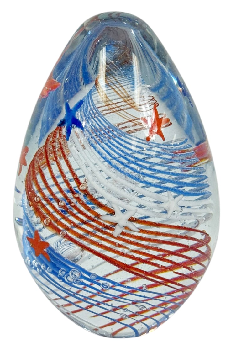 Patriotic Red, White & Blue Art Glass Paperweight: Hand blown art glass paperweight with red white and blue spiral lattice design and applied star motifs. The clear glass form contains controlled air bubbles and layered colored canes arranged in a swi