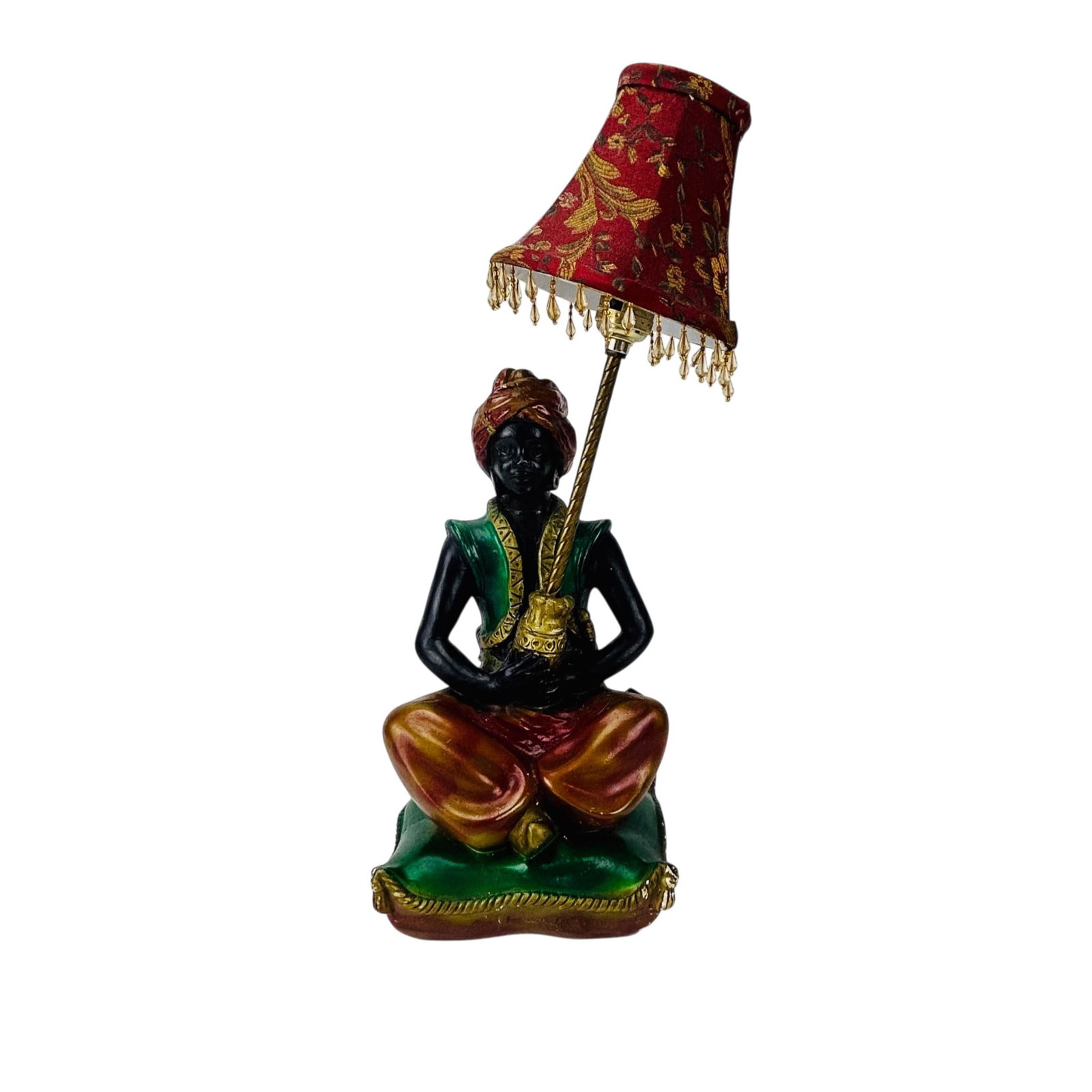 Mid Century Seated Blackamoor Nubian Table Lamp: Mid Century Modern figural table lamp modeled as seated Blackamoor figure holding a staff supporting a light fixture. Polychrome surface with black, green, red, and gilt decoration. Mounted on cushion
