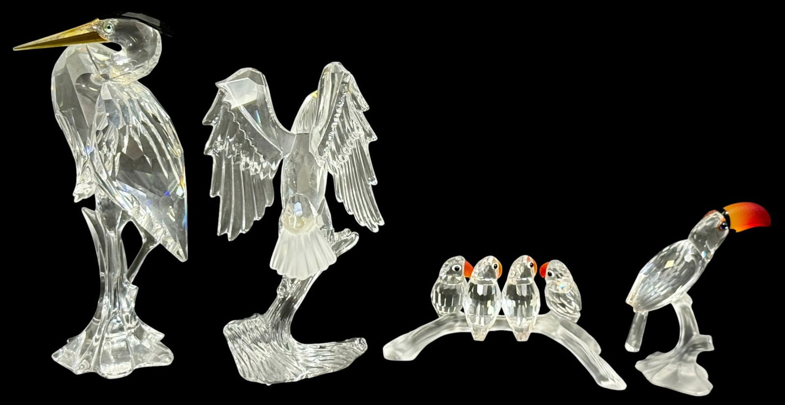 Swarovski Crystal Assorted Bird Figurines 4pc LOT: Swarovski, a group of four crystal bird figurines including a toucan, heron, eagle with wings spread, and four birds perched on a branch. Each figure is formed in clear faceted crystal with colored
