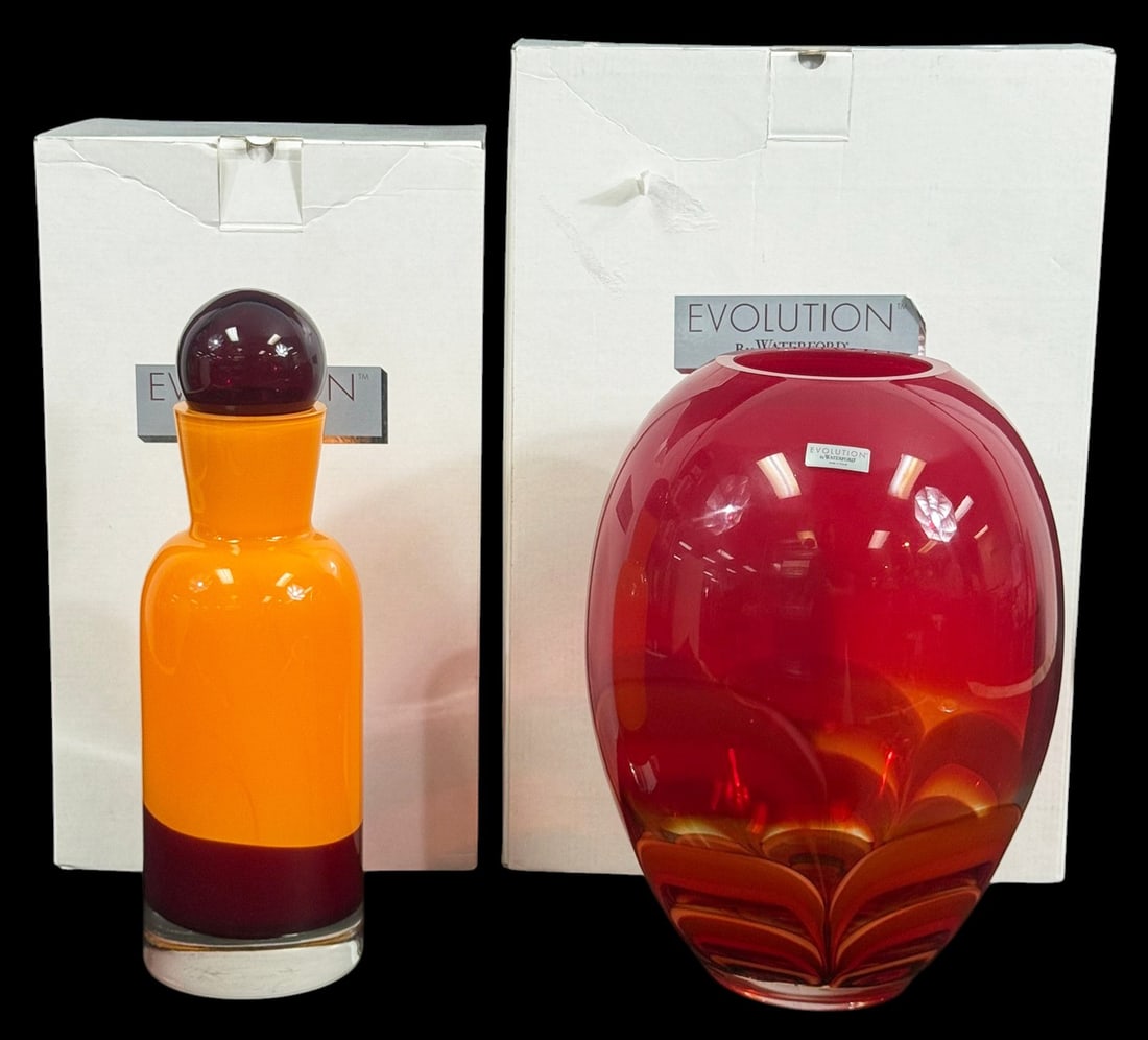 Waterford Evolution Amber Glass Vase & Decanter: Waterford Evolution, a red and amber art glass vase and decanter set. The lot includes an 11-inch ginger vase and a 12-inch decanter with stopper, both showing layered red and amber coloration. Each