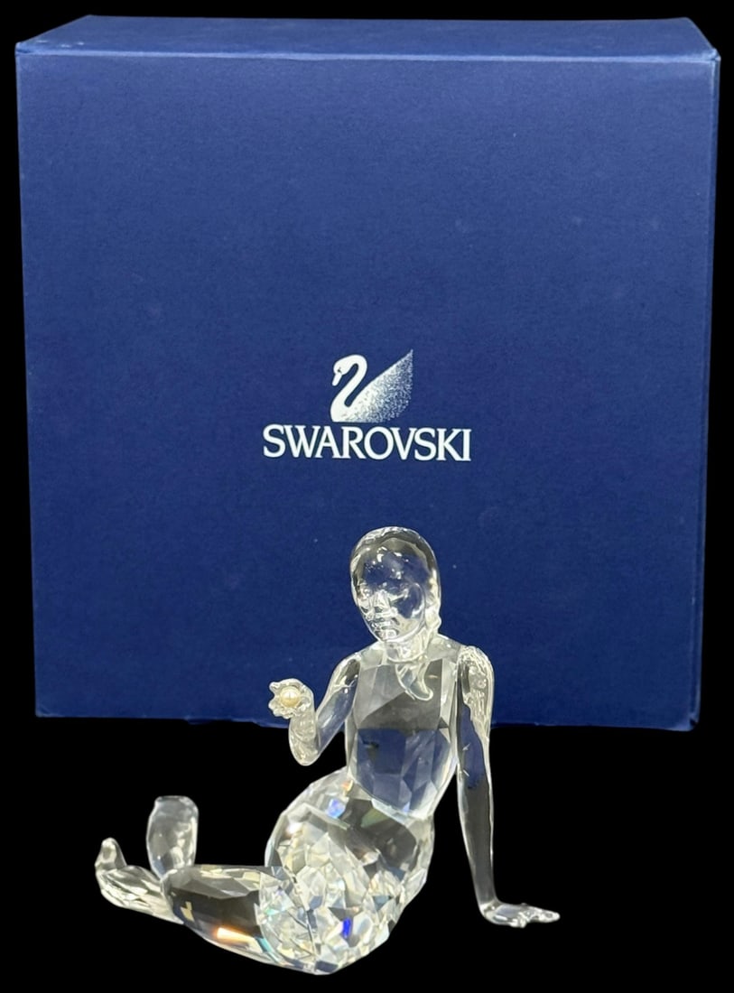 Swarovski Crystal Seated Mermaid Figurine w/ Box: Swarovski crystal figurine depicting a seated mermaid figure holding apearl. The figure is formed in clear faceted crystal with a stylized modern design. Marked Swarovski and presented in the