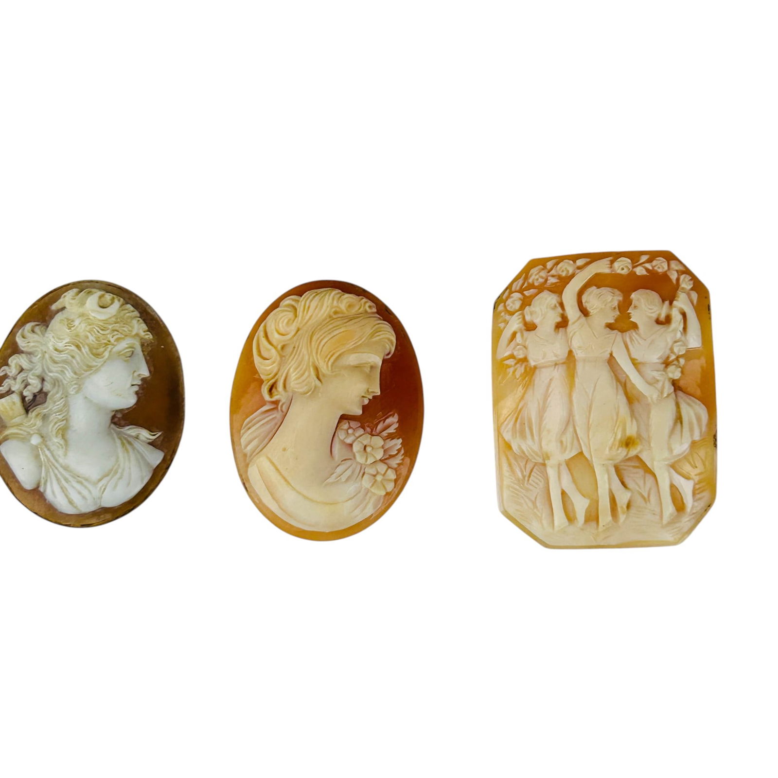 Victorian Carved Shell Portrait Maidens Cameo LOT: Group of three carved shell cameo plaques depicting classical figures in relief. Includes two oval female profile portraits and one rectangular example showing three dancing maidens beneath floral gar