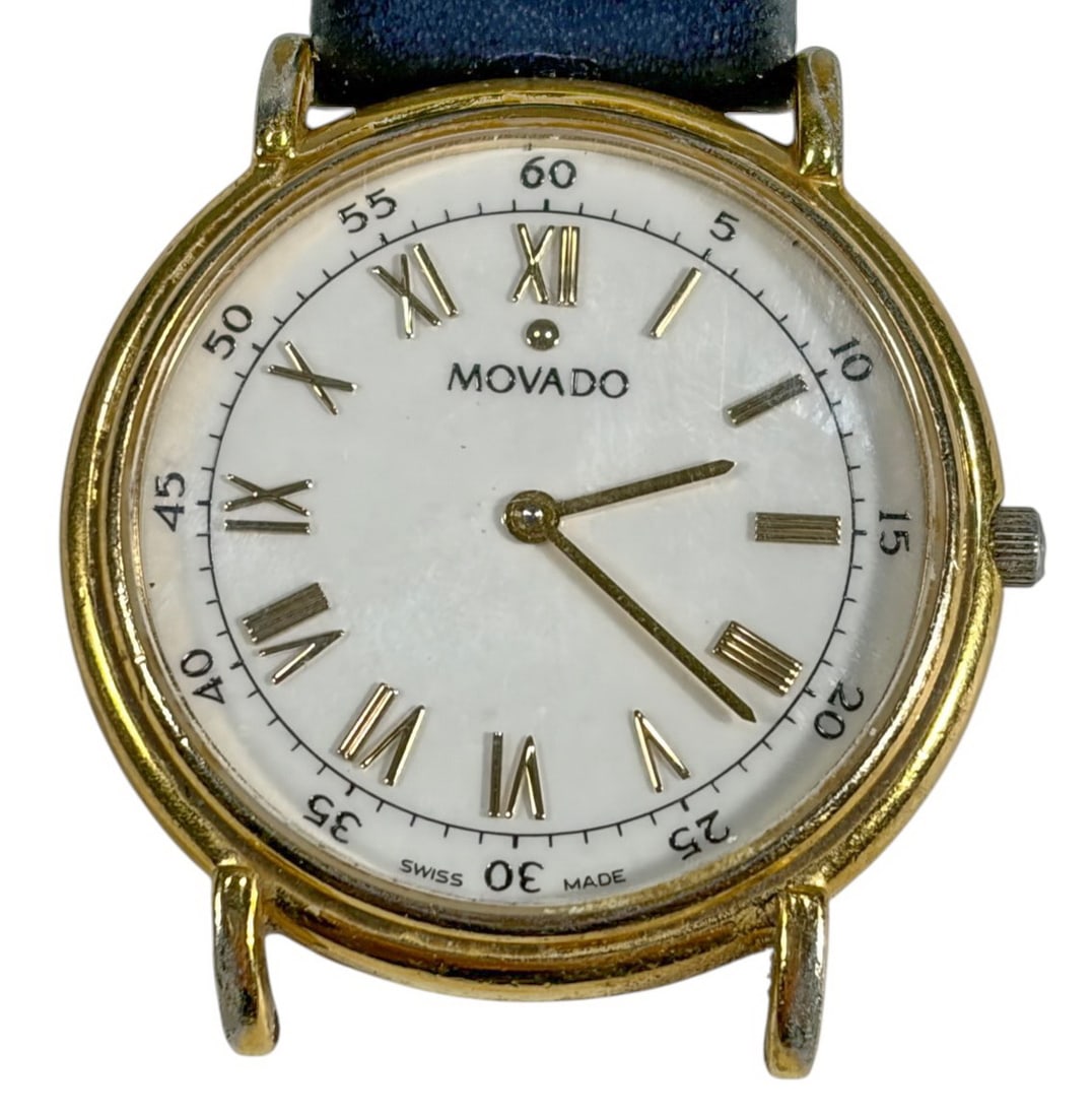 Movado Sapphire Crystal Wristwatch Gold Tone Case: Movado wristwatch with gold tone case, white dial, Roman numeral markers, and sapphire crystal, signed Swiss Made. Stainless steel back engraved with reference 87-E4-0885, fitted with black leather st