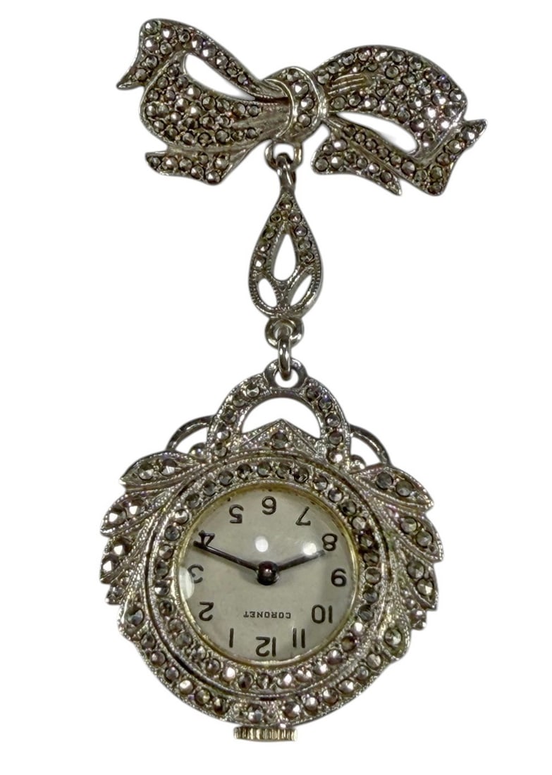 VTG Coronet Stainless Watch & Sterling Brooche: A vintage Coronet stainless steel ladies watch integrated into a sterling silver brooch with marcasite stones. The circular watch case is framed by ornate scrolling and leaf form elements. Total weigh