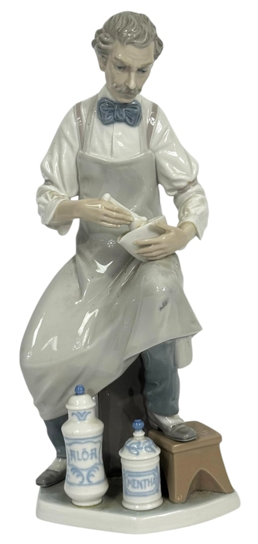 Lladro Pharmacist Type 175 Porcelain Figure #4844: Lladro Spanish modeled porcelain figurine depicting a pharmacist at work, seated and preparing a mixture with mortar and pestle. The figure is dressed in a white apron with a blue bow tie, accompanied