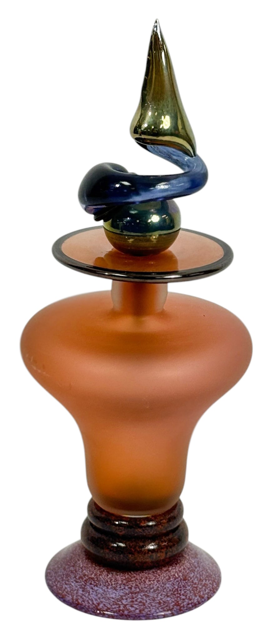 Studio Art Glass Factice Perfume Bottle w/ Stopper: Vintage studio art glass, a decorative factice perfume bottle featuring a frosted orange bulbous form with flared rim, set on a mottled purple and brown base. Topped with an elaborate hand blown stopp