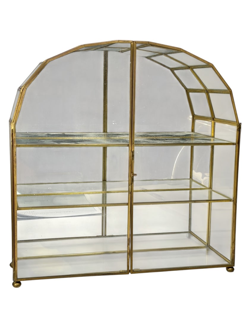 Vintage Brass & Glass Wall Vitrine Display Cabinet: Brass and glass miniature wall vitrine cabinet with arched top, glass panels and shelves, hinged front doors, brass tone frame, and rear mounting hooks.Dimensions: 13.75 X 13.25 X 4 in. Condition: