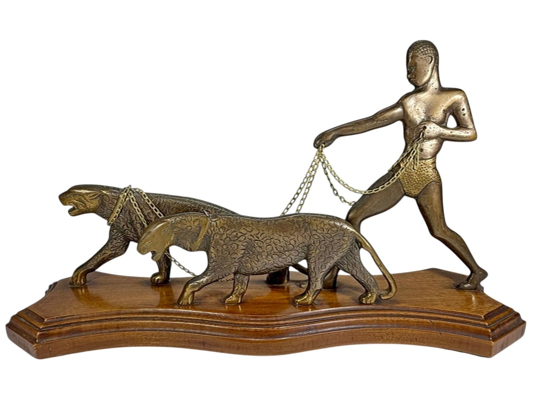 Art Deco Bronze Figural Sculpture On Wood Base: Cast bronze figural group of nude male handler with two stylized big cats on chain leashes, dynamic Art Deco form with elongated bodies, mounted on a stepped wooden base. Dimensions: 10.375 X 18.25 X 