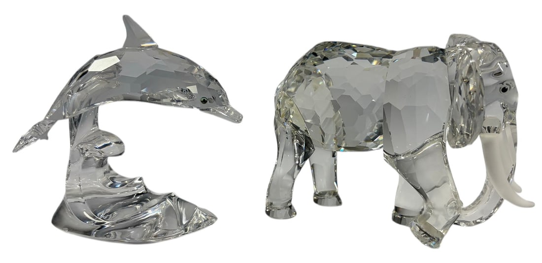 Swarovski Crystal Elephant & Dolphin Figurines 2pc: Lot of two Swarovski faceted crystal animal figurines, including an elephant and a dolphin. The elephant features frosted tusks and faceted body, while the dolphin is modeled leaping over a stylized w
