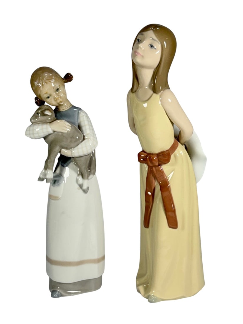 Lladro Girl w/ Lamb & Naughty Girl w/ Hat Fig 2pcs: Lladro Spain, pair of glazed porcelain figurines of a girl holding a lamb and a standing girl with hat, soft pastel tones. Both are marked 'Hand Made in Spain.' The largest measures approximately 9.75