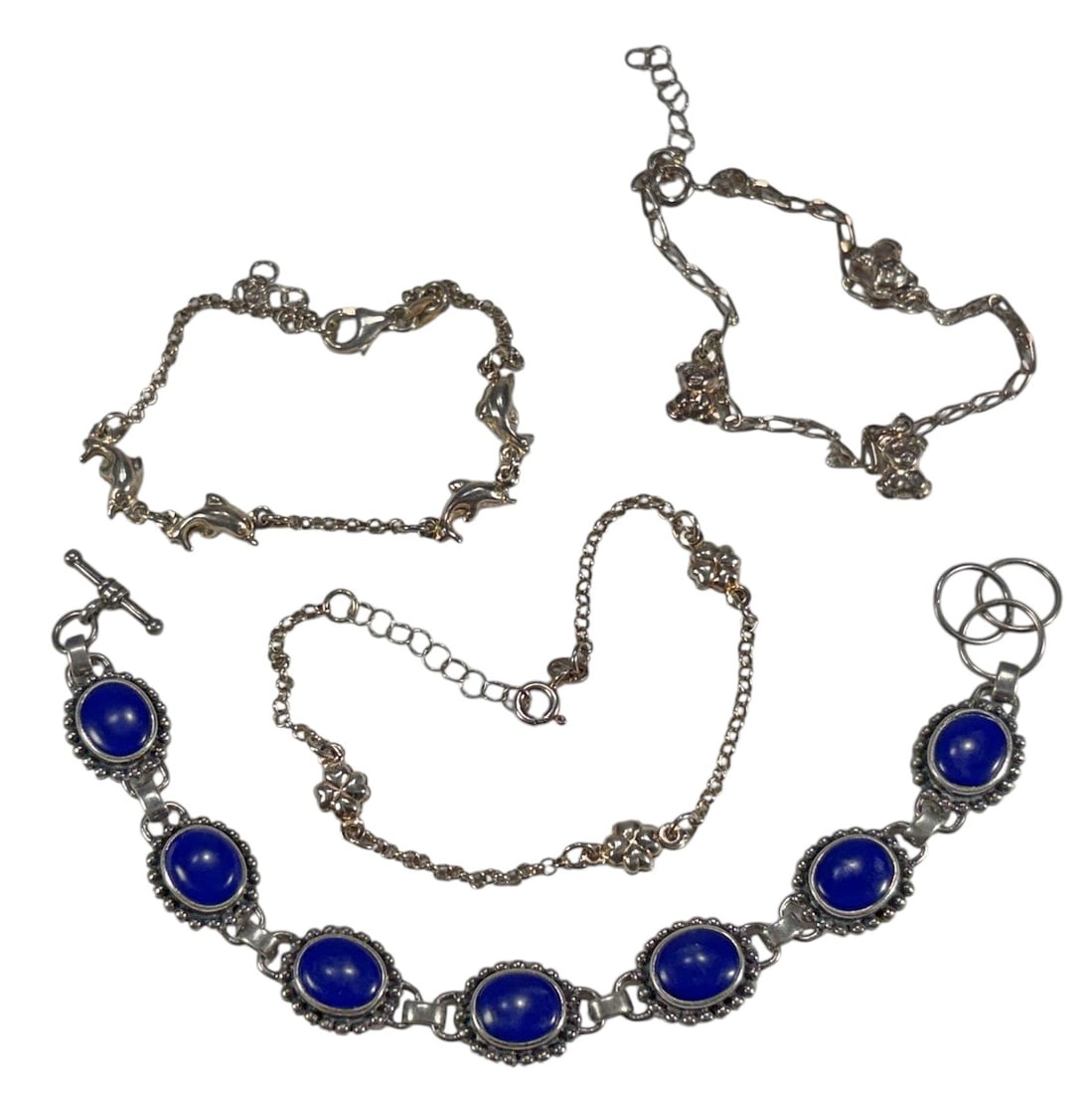 Sterling & Blue Stone & Mixed Metal Bracelets 4pcs: Group of four bracelets including one sterling silver (marked 925) example set with oval blue stones and three yellow metal chain bracelets with decorative elements including teddy bears, dolphins, an