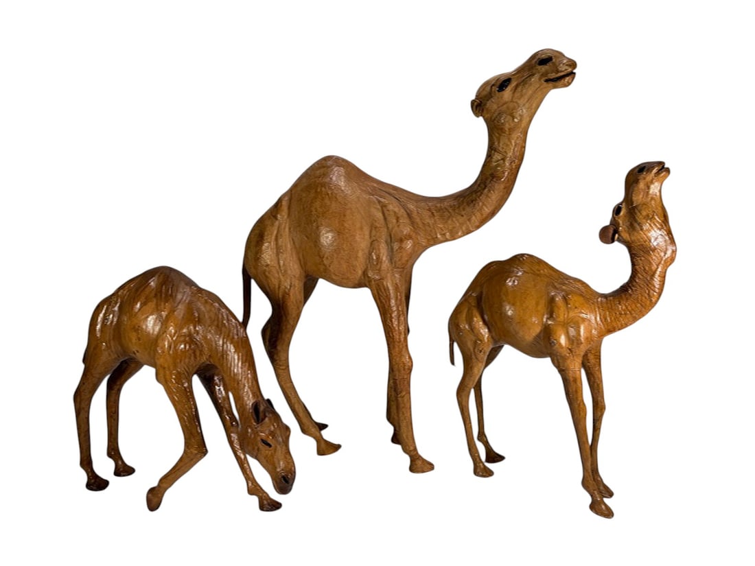 Camel Leather Covered Figurative Sculptures 3pcs: Set of three leather covered camel sculptures, each modeled in naturalistic form with elongated legs and stylized features, including one grazing, one standing, and one with raised head. The largest m