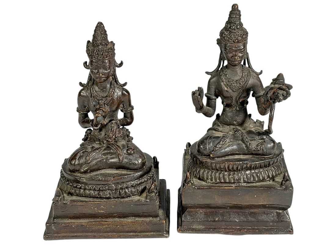 Pair Asian Bronze Seated Deity Figures Lotus Bases: Cast bronze figural group depicting two seated deities in cross legged posture atop tiered lotus bases, each figure wearing ornate headdress and jewelry, one holding a lotus stem and the other in a ge