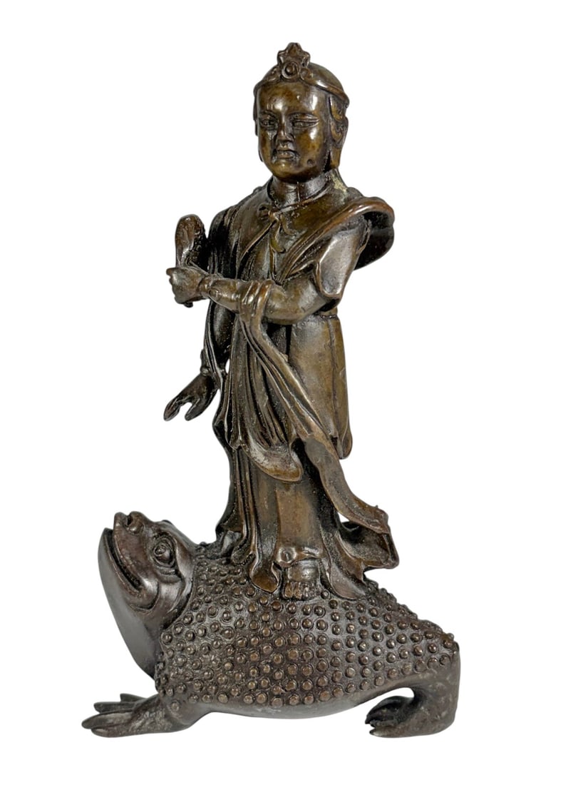 Asian Style Bronze Child Figure On Toad Sculpture: Cast bronze figure depicting a robed child standing atop a stylized three-legged toad with textured back and upturned head, the child holding an object in one hand and draped garments flowing along th