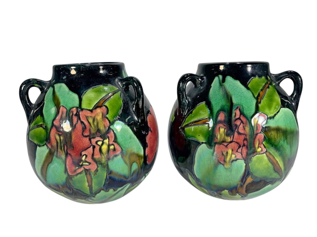 Pair of Art Nouveau Style Glazed Pottery Vases: Pair of ceramic vases with twin handles and rounded bodies, decorated in an Art Nouveau style with raised floral motifs in green and red tones against a black ground. Each piece measures approximately