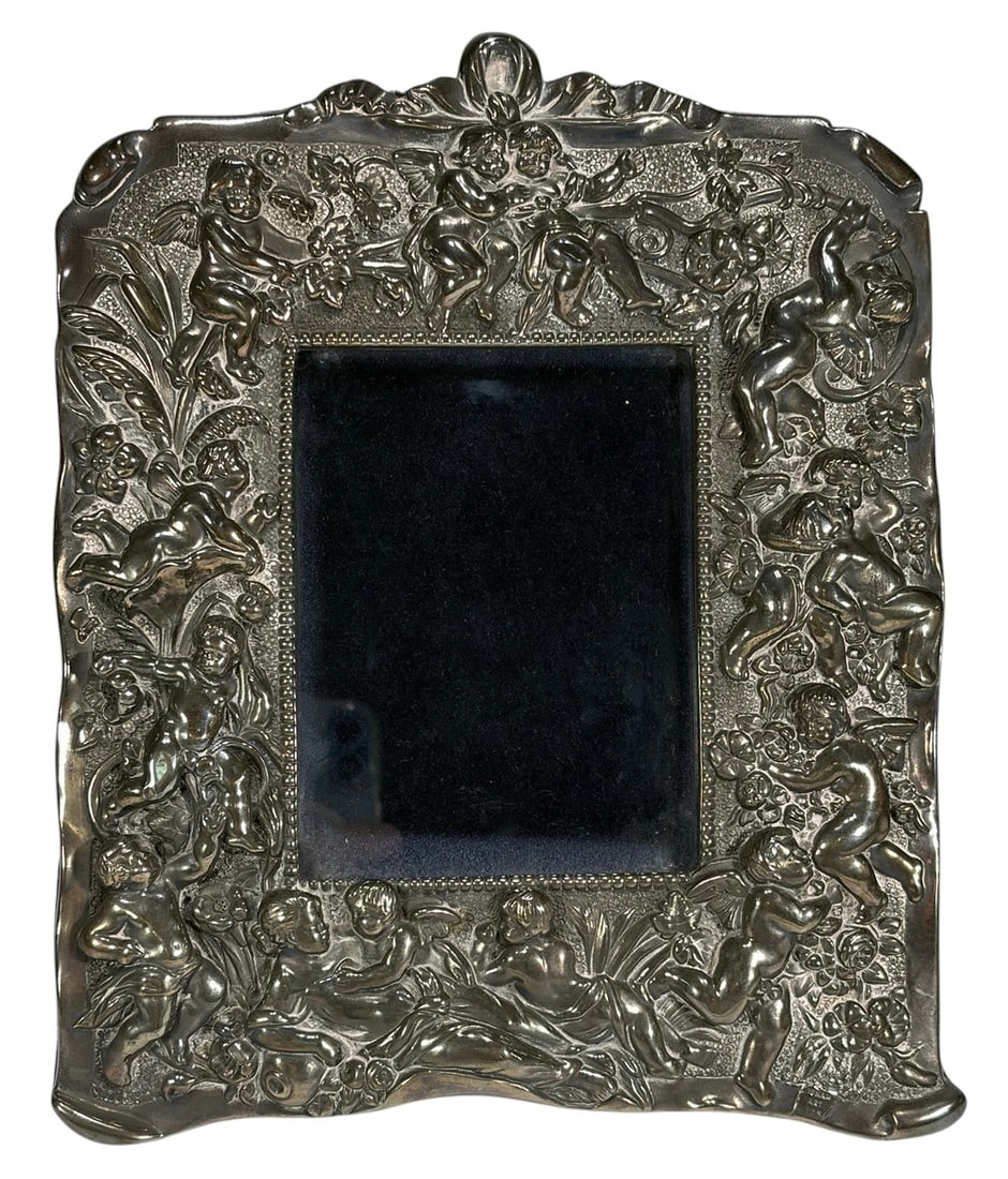 Isham Art Sterling 925 Cherubs Picture Frame: Isham Art sterling silver 925 cherub picture frame, high relief putti and scrolling foliate border, beaded inner edge, blue velvet backing with easel support, marked 'Isham Art 925.' Frame measures ap