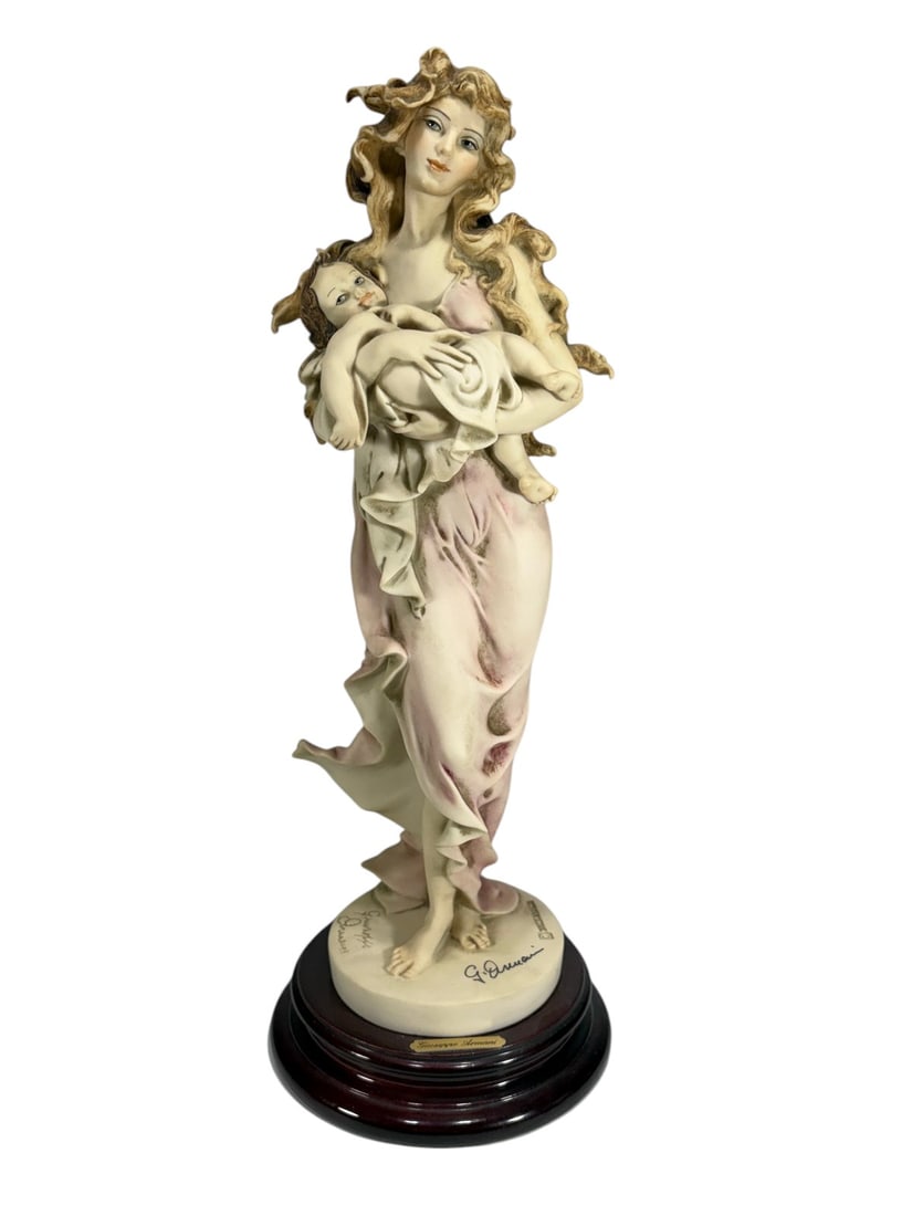 Giuseppe Armani Loving Arms 880E Female Figure: Giuseppe Armani figurine titled 'Loving Arms,' model 880E. Depicts a female figure holding a child, executed in soft pastel tones with flowing drapery. Mounted on original round wooden base with metal