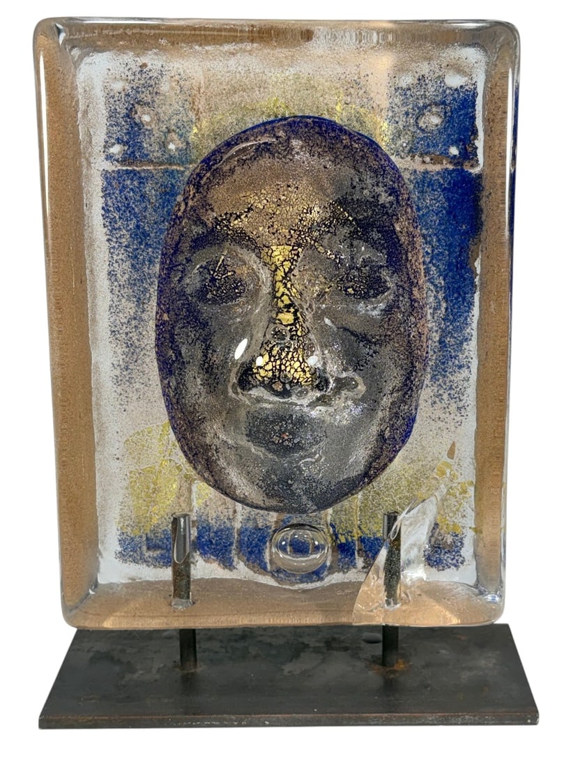 Bertil Vallien for Kosta Boda Face Glass Sculpture: Contemporary art glass face sculpture by Bertil Vallien for Kosta Boda, depicting a stylized mask form in clear, blue, gold, and smoky tones, mounted on a metal stand. Dimensions: 9.75 X 7 X 2.75 in. 