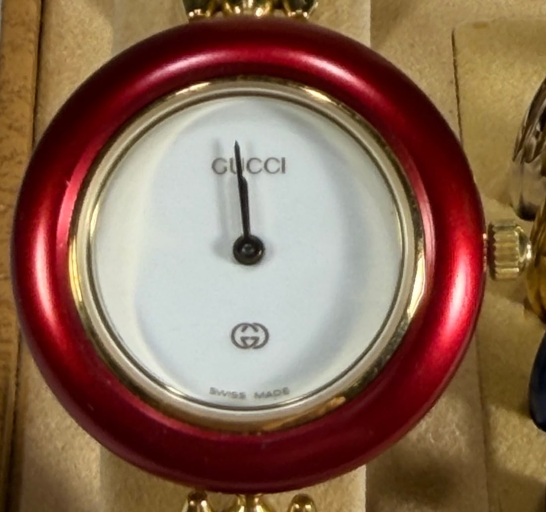 Gucci 11/12 Change Bezel Gold Tone Wristwatch: Swiss made Gucci 11/12 women's quartz wristwatch featuring a white dial with gold tone bracelet and interchangeable colored bezels. Watch case measures approximately 16 mm. Includes multiple bezel col
