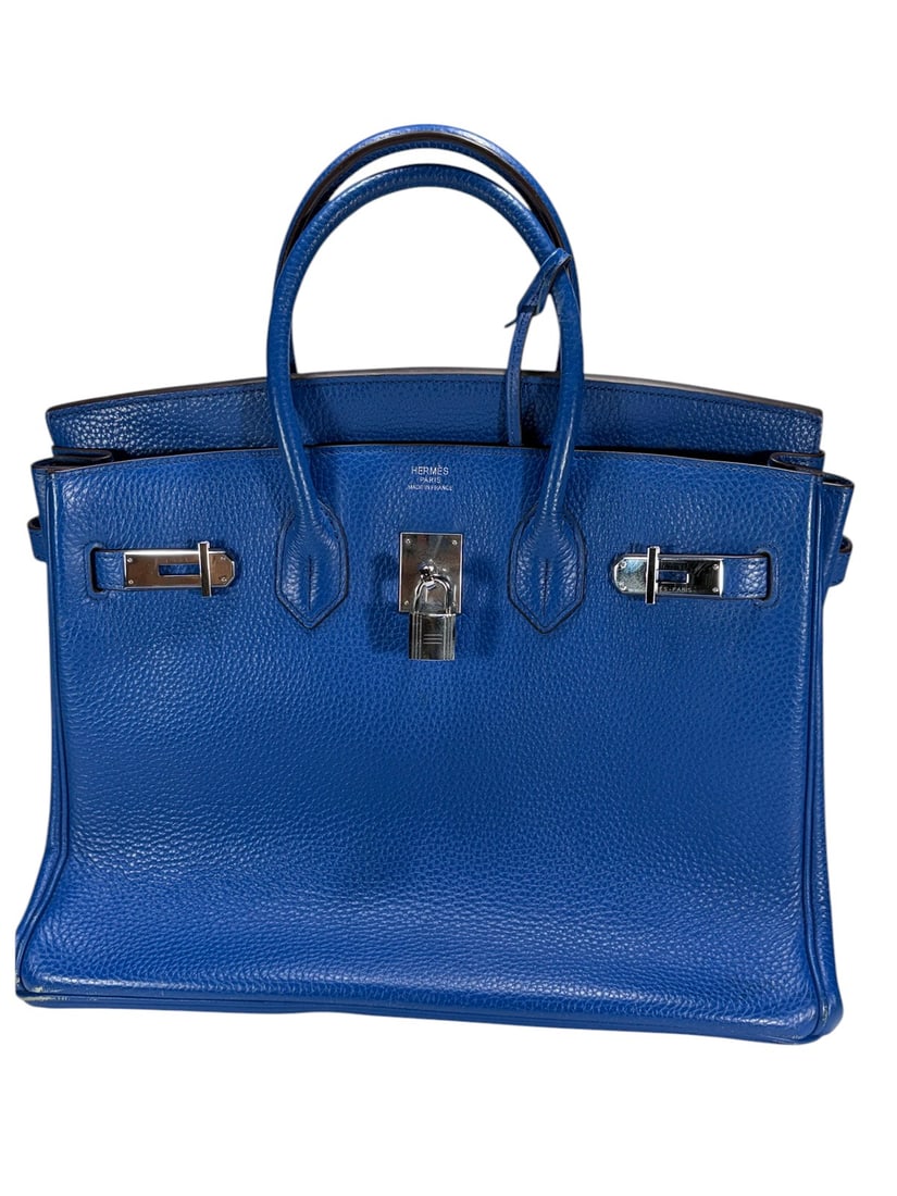 Blue Textured Faux Leather Birkin Style Handbag: Blue leather-like textured handbag in Birkin style featuring rolled handles, flap top closure, lock and clochette, and silver-tone hardware. Interior with center zip compartment and side pockets.