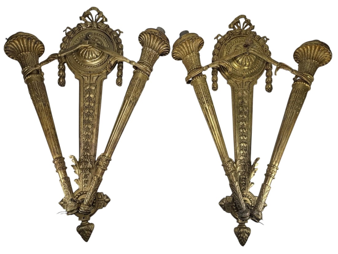 Large Pair French Style Gilt Bronze Wall Sconces: Pair of French style bronze wall sconces with gilt patinated finish and elaborate neoclassical decoration. Each features double fluted torch-form candle arms, foliate garlands, ribbon crest and ornate