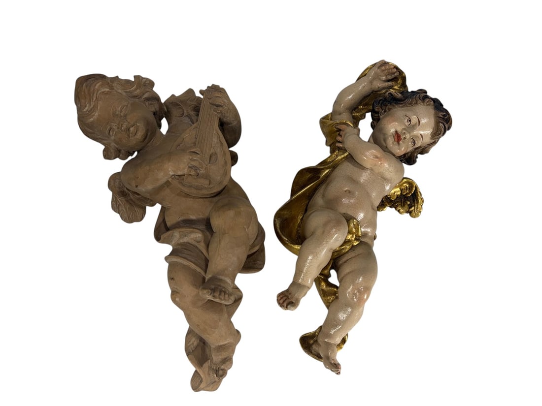 20th Century Wooden Cherub Sculptures 2pc LOT: Pair of twentieth century carved wooden cherub wall sculptures. One figure depicts an angel playing a lute with natural unfinished wood surface, the other features painted and gilt decoration with flo