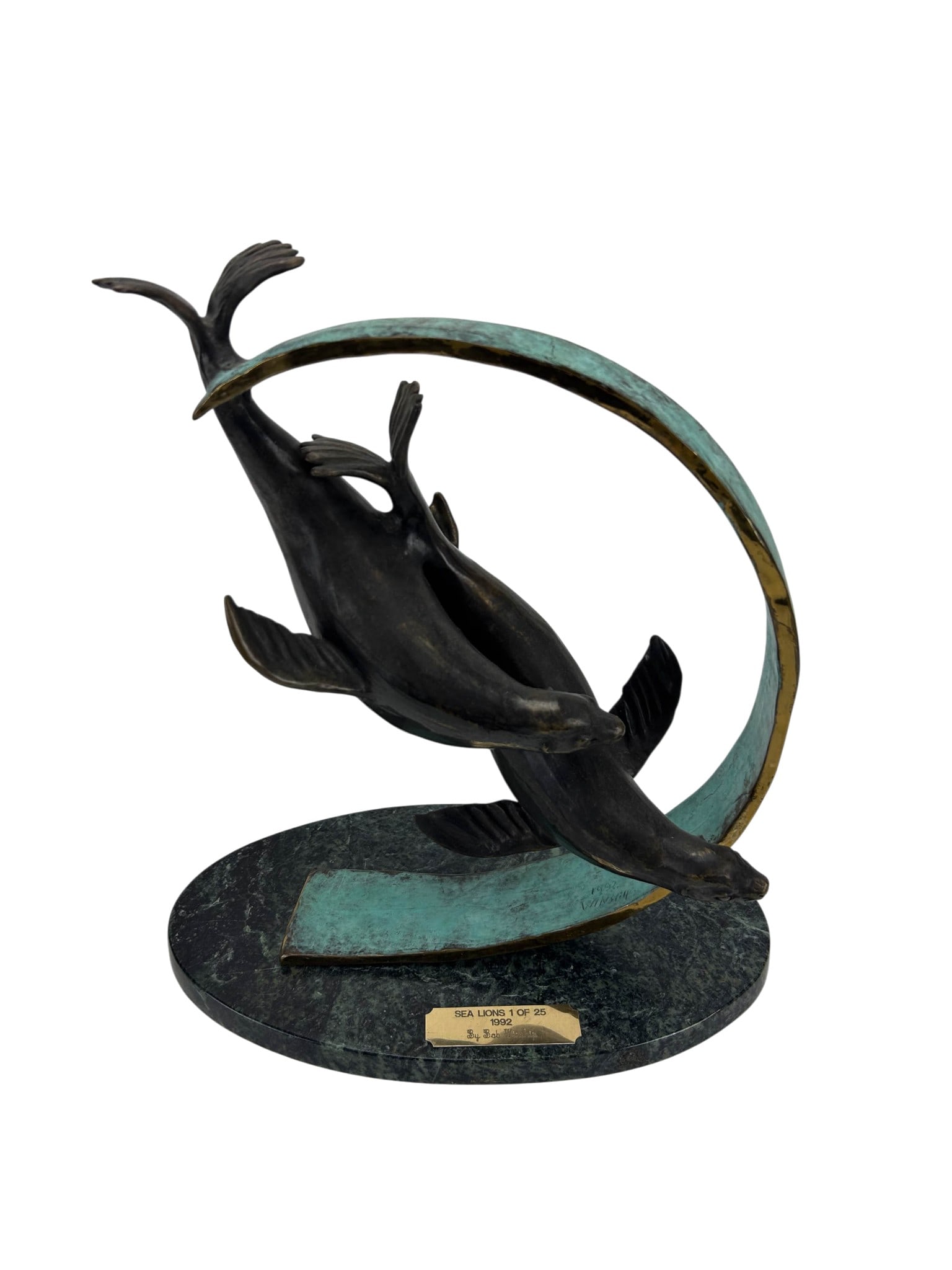 Bob Winship 1927-2019 Sea Lions Bronze Sculpture: Bob Winship ((American, 1927-2019) bronze sculpture depicting two sea lions in motion within a sweeping wave form element. Dark patinated bronze with verdigris accents, mounted on an oval marble base