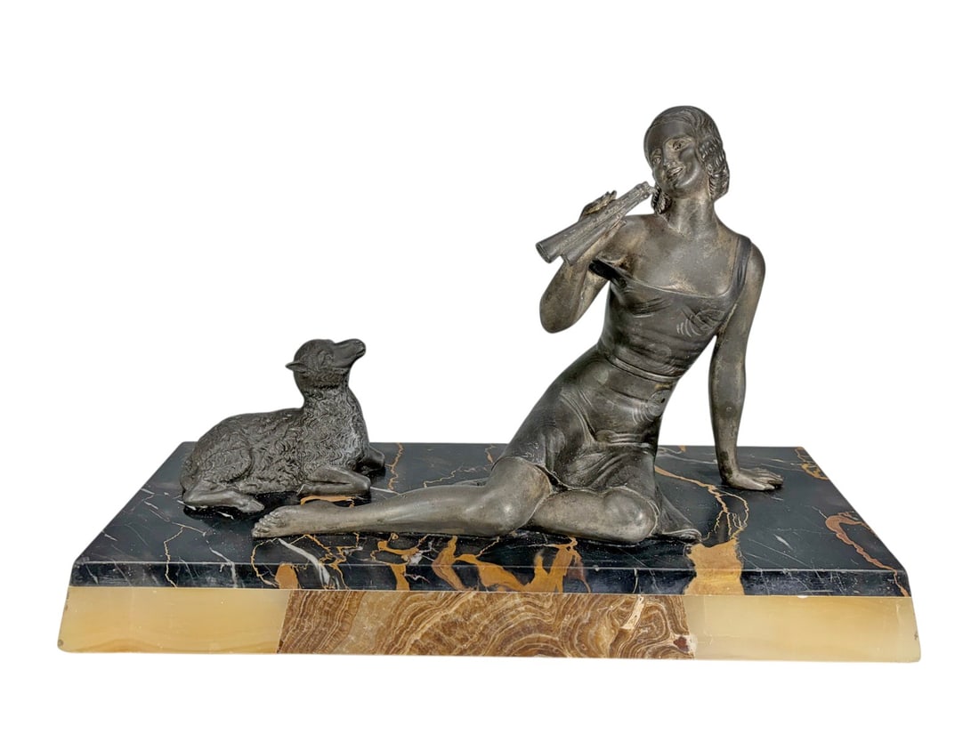 Art Deco Style Signed Metal Woman & Lamb Sculpture: Art Deco style figural sculpture depicting a seated young woman holding a flute and accompanied by a reclining lamb. Executed in patinated metal with a dark bronze-tone finish, the sculpture is mounte