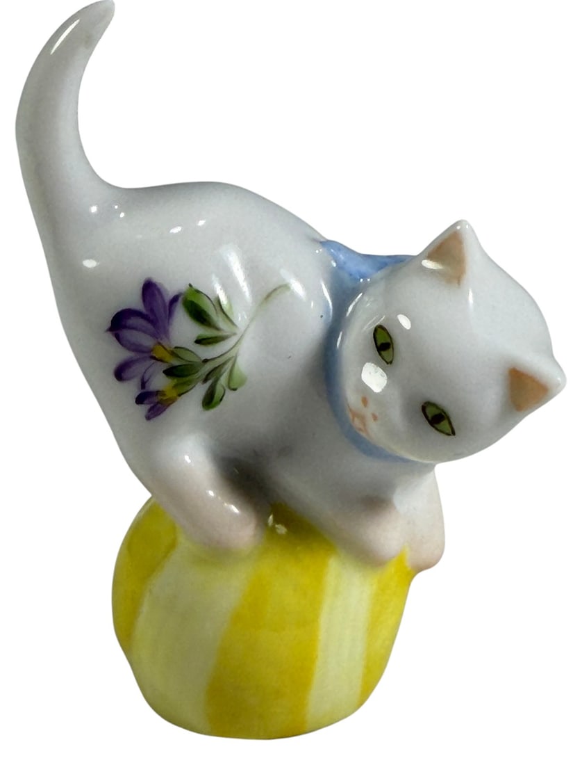 Herend Hungary Porcelain Cat on Yellow Ball Fig: Hand painted Herend Hungary porcelain figurine depicting a white cat with green eyes and blue bow collar balancing atop a yellow ball. The cat is decorated with delicate floral sprays in pink and purp