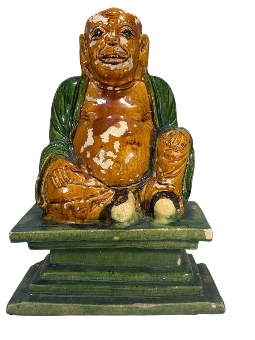 Chinese Sancai Style Glazed Pottery Budai Figure: Chinese pottery figure of Budai, the Laughing Buddha, seated on a stepped plinth. Decorated in amber-brown and green sancai-style glazes with exposed belly and smiling expression. Shows extensive glaz