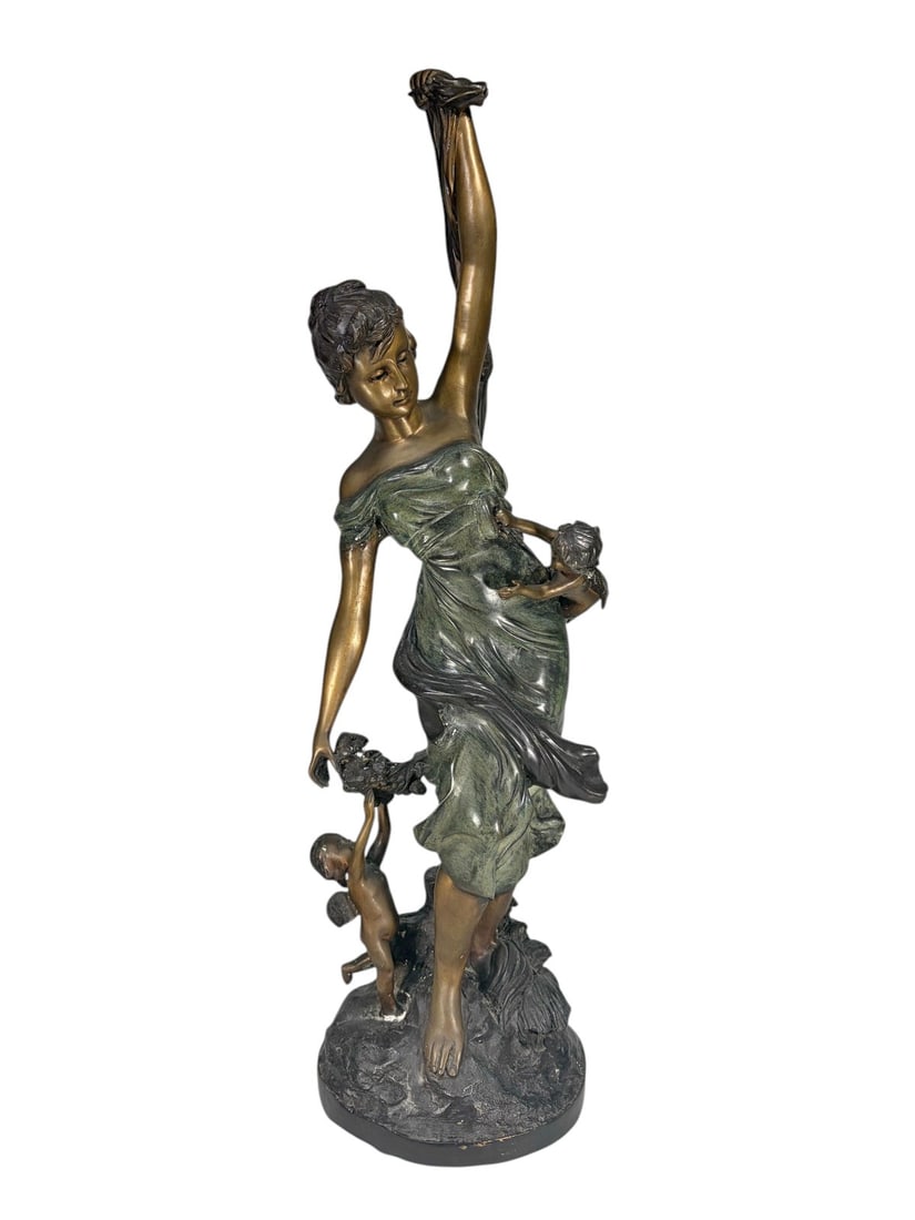 Bronze Art Nouveau Style Figural Maiden Sculpture: Bronze Art Nouveau Style figural sculpture depicting a maiden in flowing drapery with raised arm, accompanied by cherub figures and floral elements. The raised arm appears intended to support a lamp, 