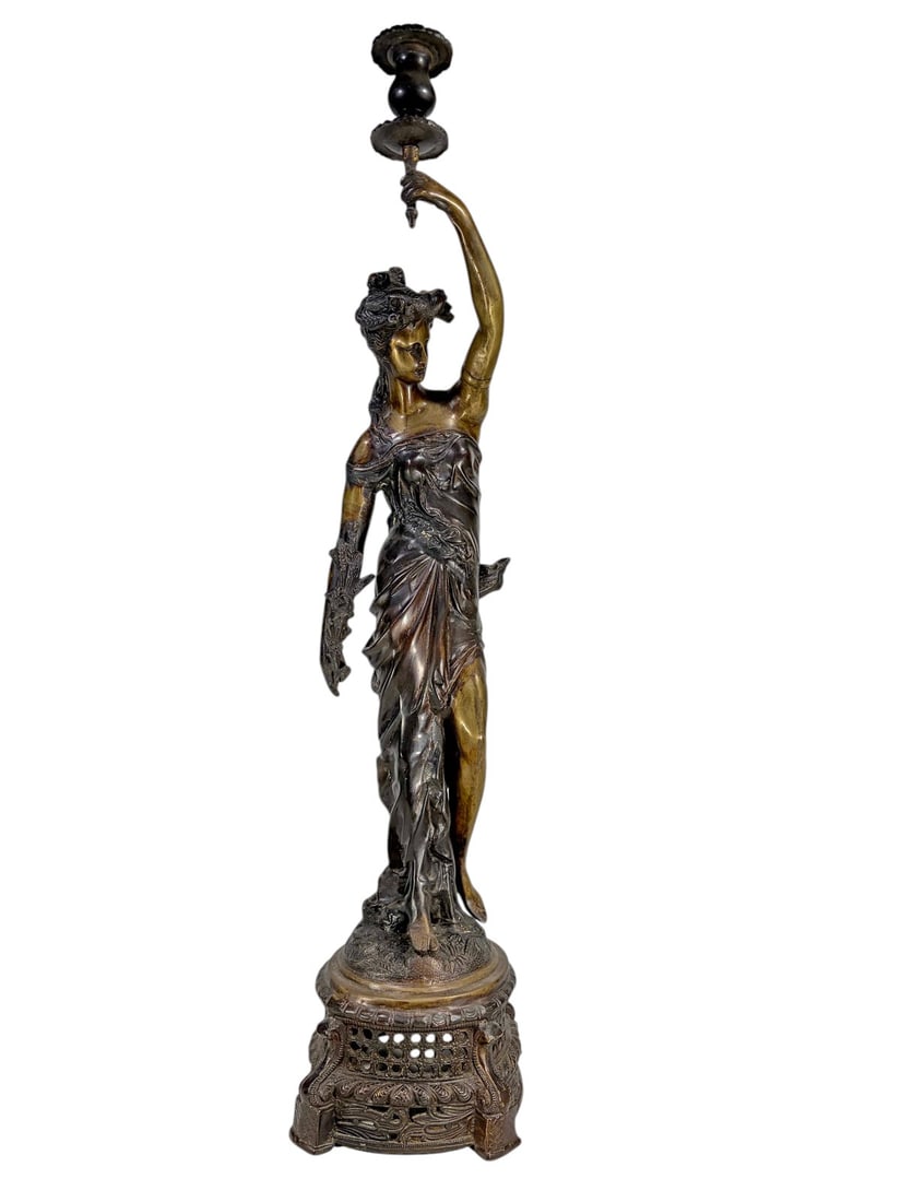 Bronze Figural Woman Candlestick Classical Decor: Bronze candlestick depicting a classical draped female figure standing on an ornate openwork pedestal base with foliate and scroll decoration. The figure supports a single candle socket with drip pan.